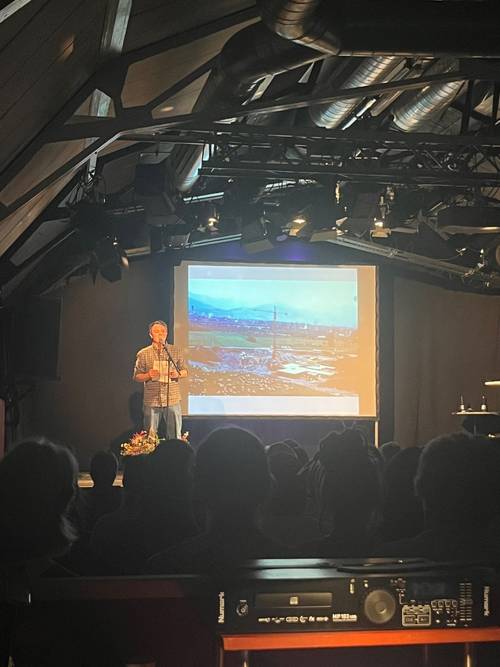 Michael Eggert auf der Bühne vor der Leinwand, auf der Bilder des Mehrgenerationenhaus geteigt wurden